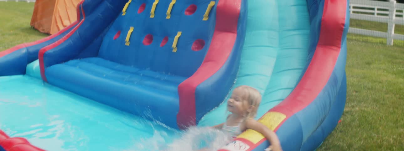 Girl in a swimsuit slides down an inflatable pool playground in the backyard