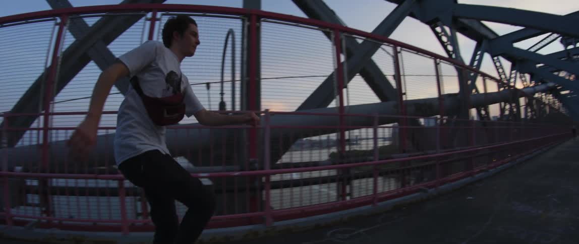 Young man skateboards on a metal bridge in the city at sunset