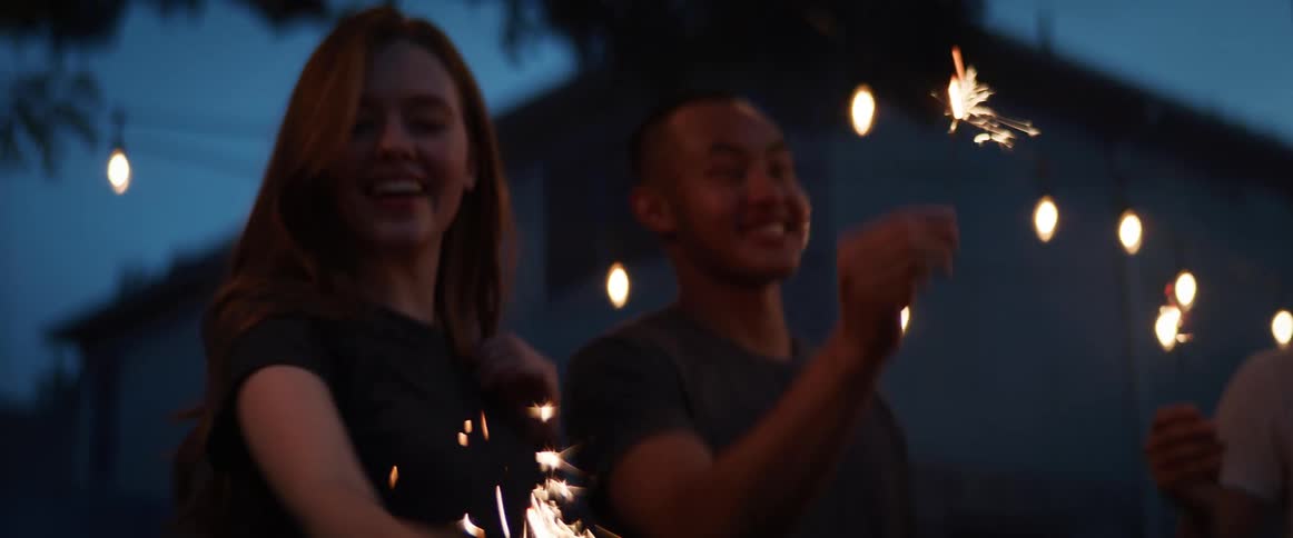 A group of young friends light sparklers in a back yard at night