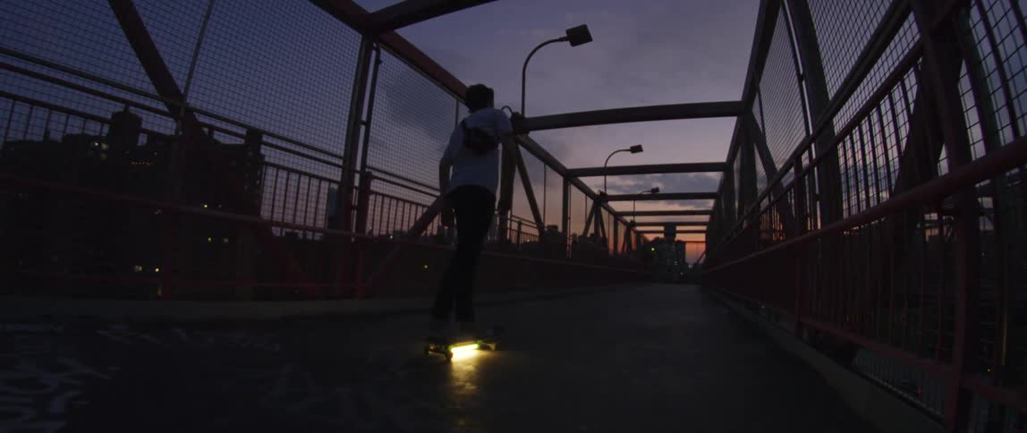A man is riding his skateboard over the bridge at dusk