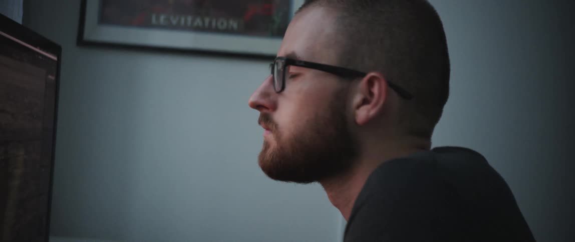 Side view of a man with a beard and glasses sitting at a desk and using a computer in a room