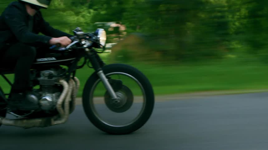 A person rides a motorcycle through a woodland during the day