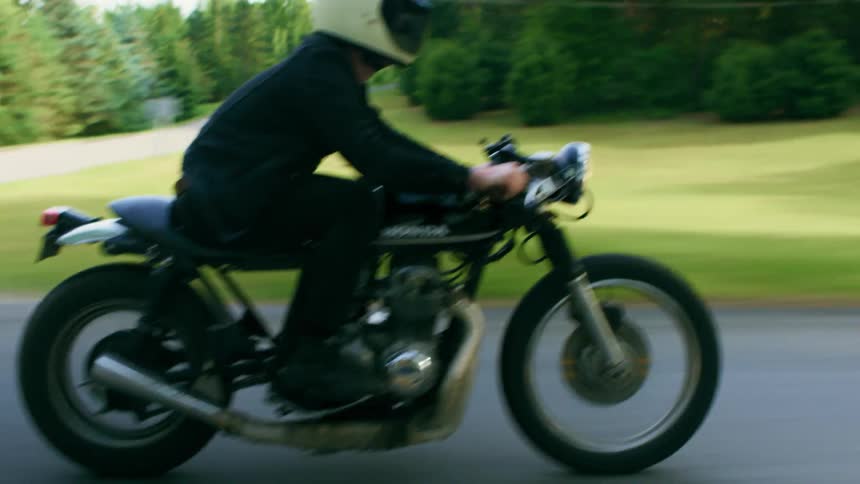 Man with a white helmet black jeans jacket rides a motorcycle on a road in the countryside