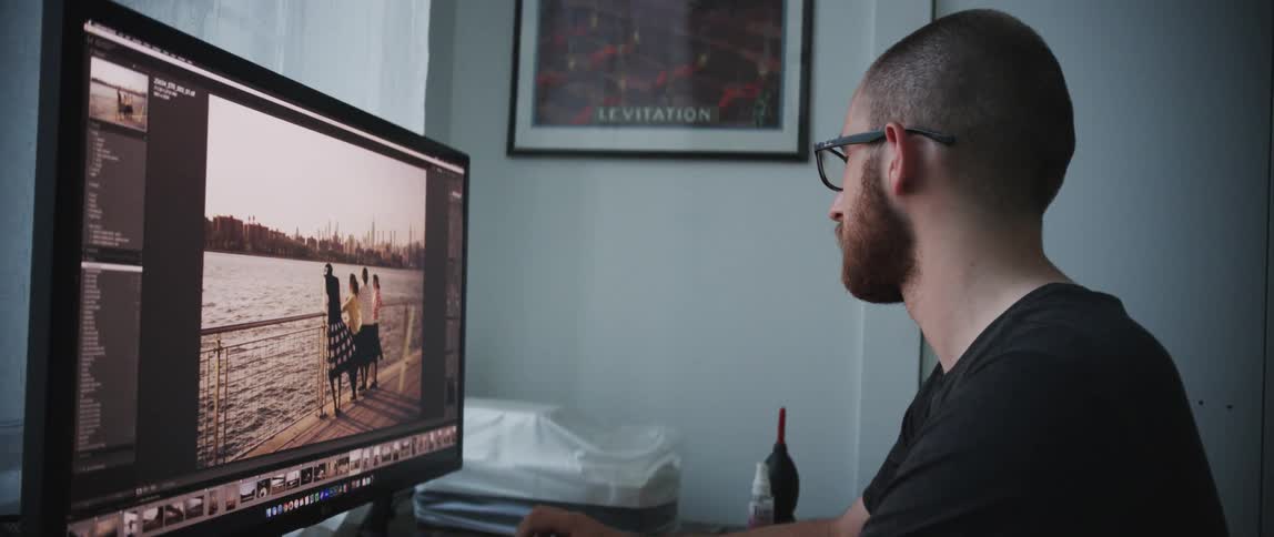 Man sits in front of a computer using editing software to modify pictures
