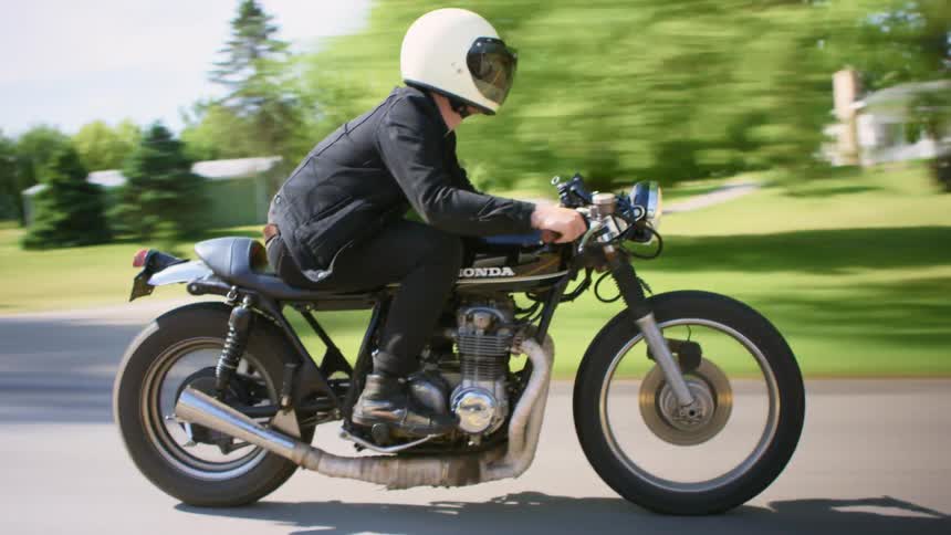 Man with a white helmet black jeans jacket rides a motorcycle on a road in the countryside