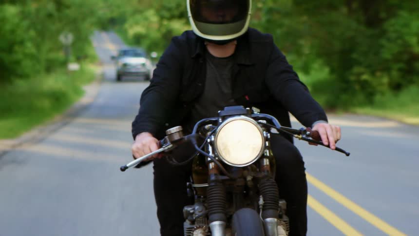 Male motorbiker with a white helmet and black jacket pants rides a motorcycle on an asphalt road in the countryside