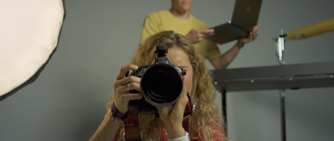 Woman takes a photo with a camera while a man carries a laptop over next to her