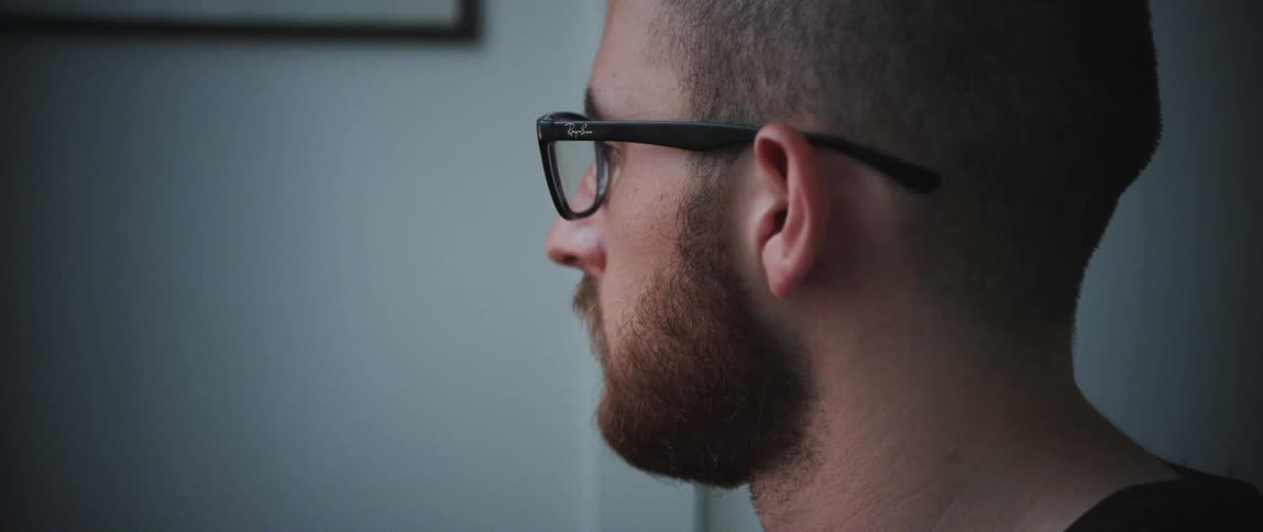 Man with a beard and glasses sitting down uses a computer in a room