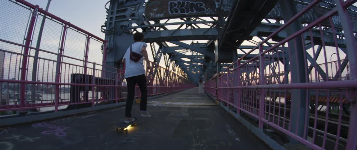 Young man skateboarding on a metal bridge at sunset