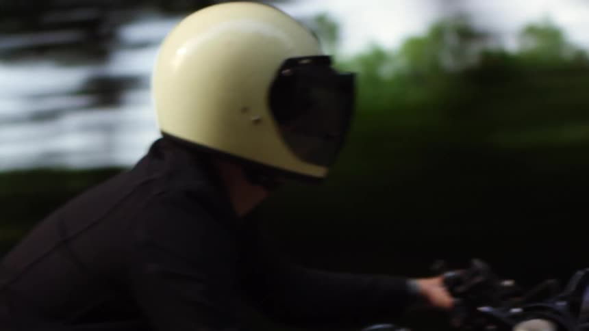 Man with a white helmet rides a black motorcycle on a country road