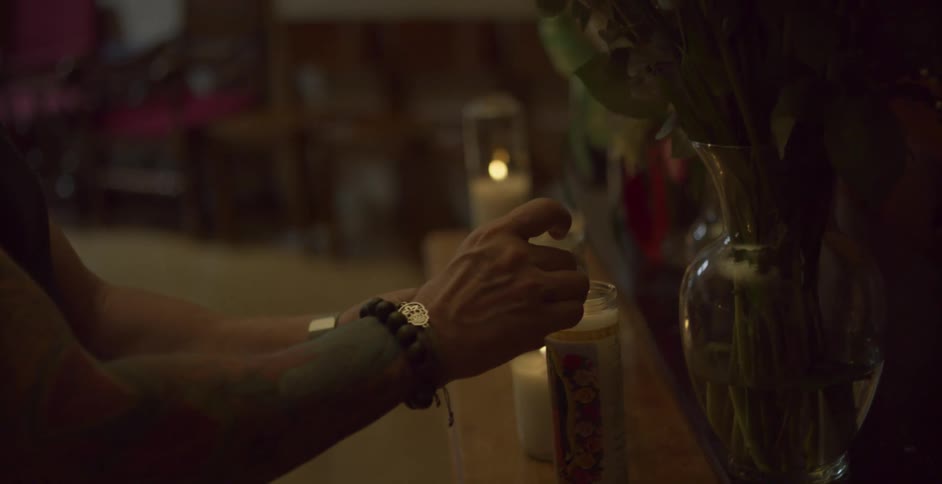 A man lights a candle in a dark room with other lit candles around on a shelf