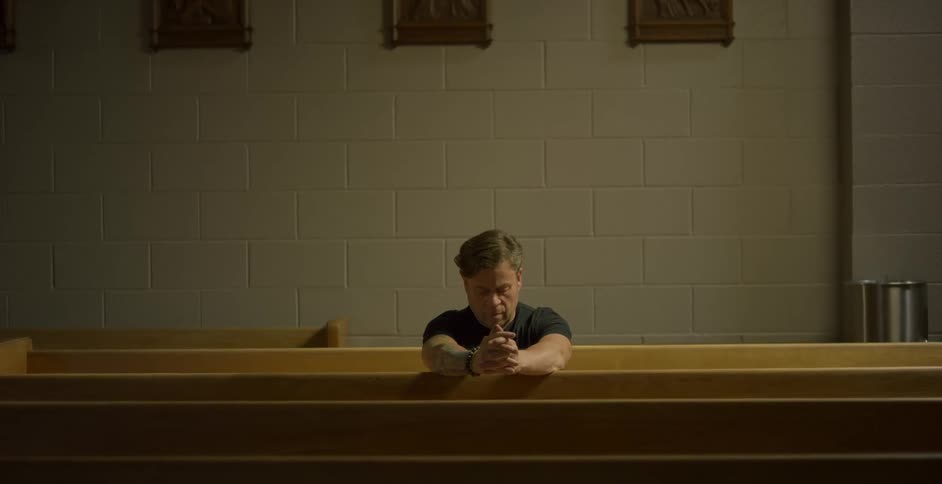 A man sits in prayer in the otherwise empty pews of a church