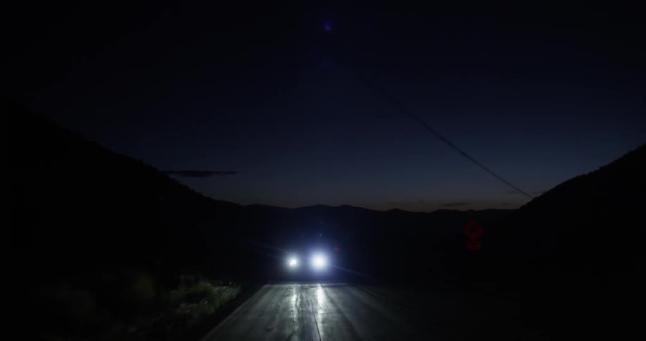 Headlights of a car as it travels along a dark road