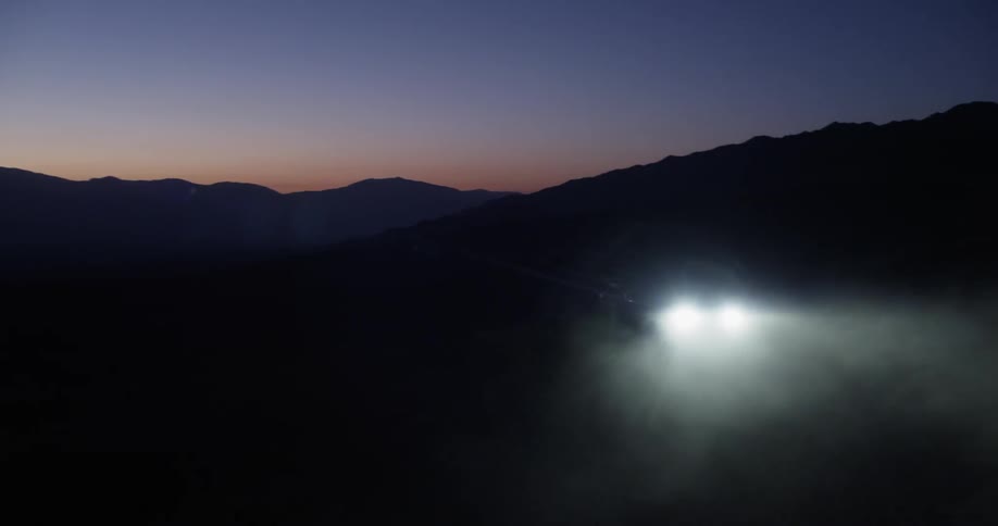 A vehicle's headlights can be seen traveling at dawn