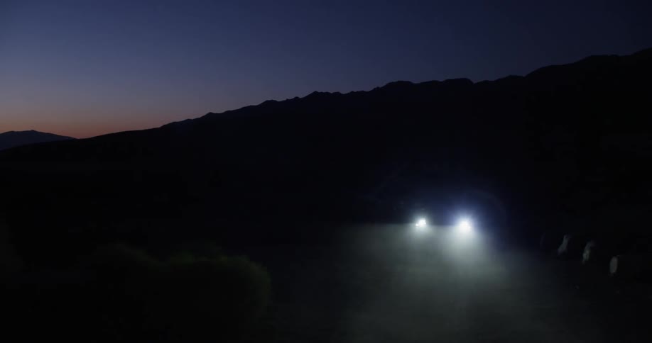 A vehicle drives on a road in the mountains at night