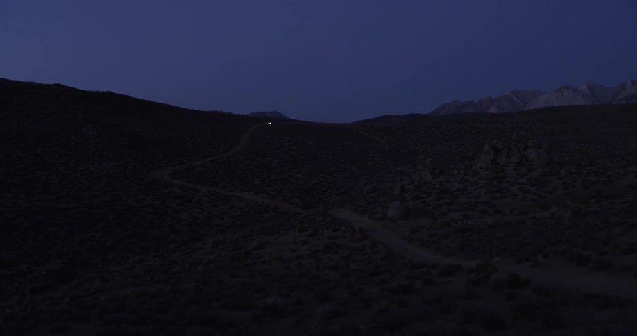 A car's lights are seen in the distance as it traverses a narrow dirt road