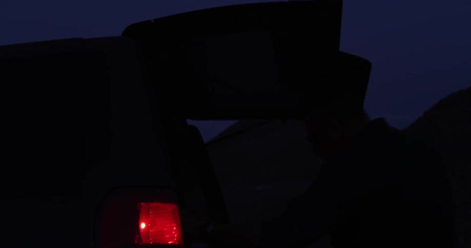 A man opens the back of his car and pulls out a rope at night