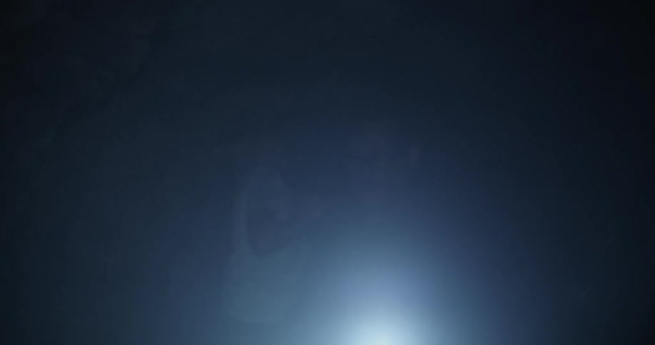 A man is holding a child as he shines a flashlight in a dark cave