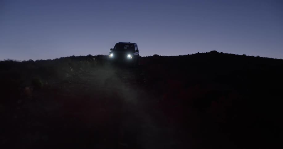 A 4 wheel drive vehicle with its lights on driving off road at dusk or dawn