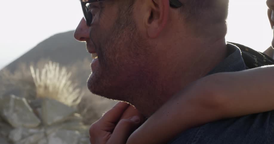 A child is hanging from a man's shoulders as they smile