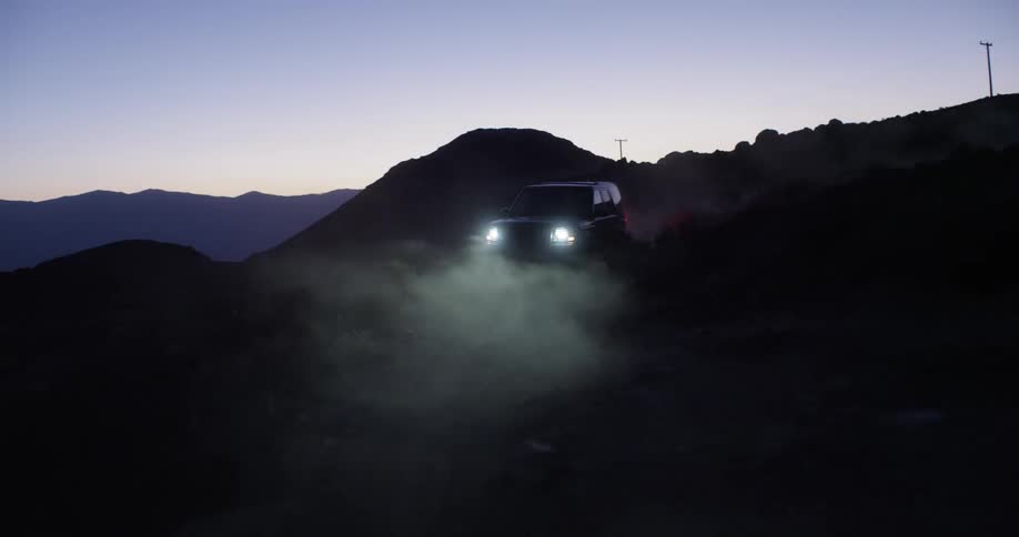 A car drives down a foggy road near sunrise with its headlights on