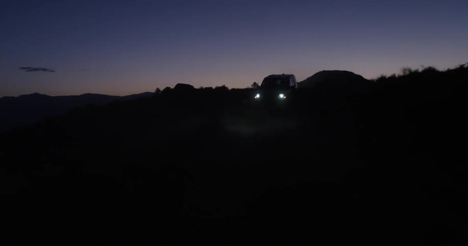 An SUV with its headlights on driving through a landscape at dawn or dusk
