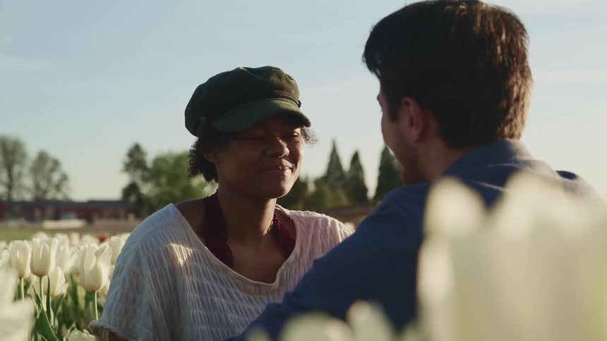 A woman and man smile at one another while sitting in a field of white flowers