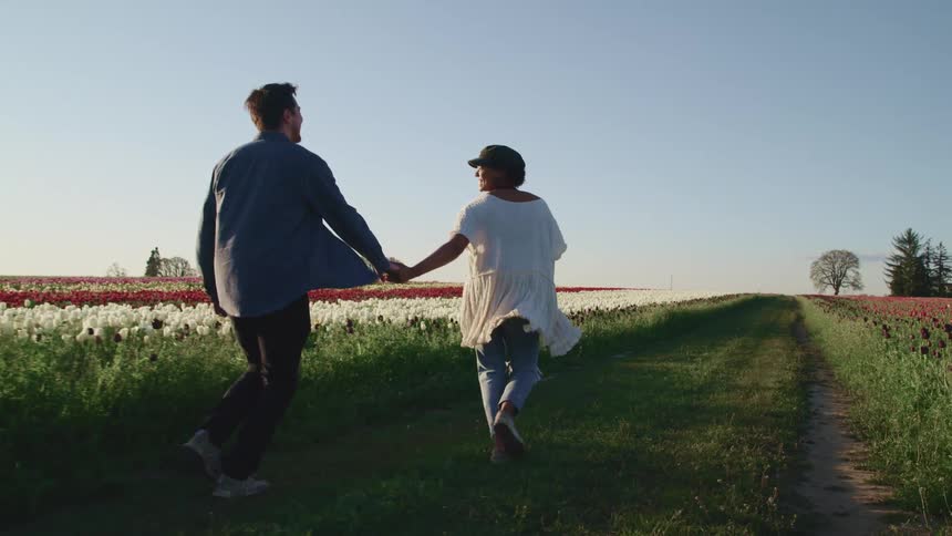 A man and woman hold hands running through a field of flowers