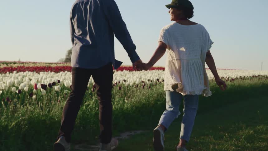 A man and woman hold hands running through a field of flowers together