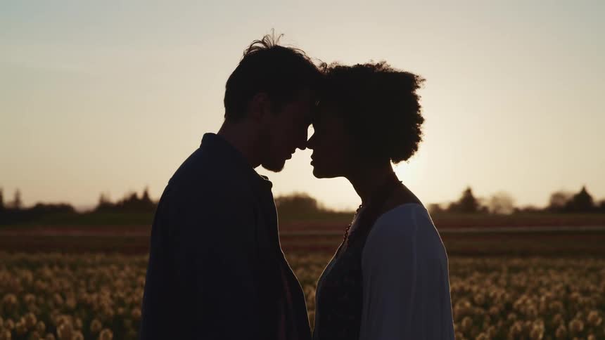 A man and woman stand in front of a field with their foreheads pressed together as they look in to one anothers eyes