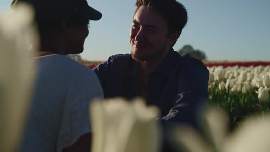 A man and woman sitting in a field of flowers smile at one another