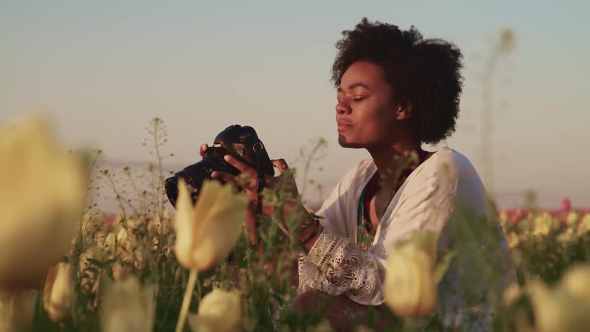 Black woman sits in a field of tulips and takes a photo with a camera