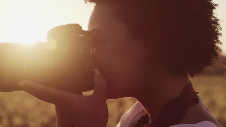 Black woman with curly hair takes photographs in tulip fields at sunset