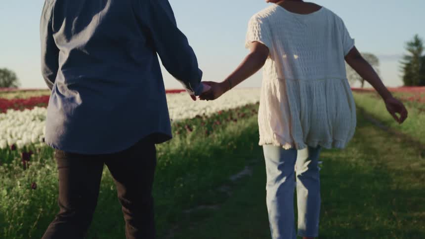 Young couple runs holding hands next to a field of tulips at sunset