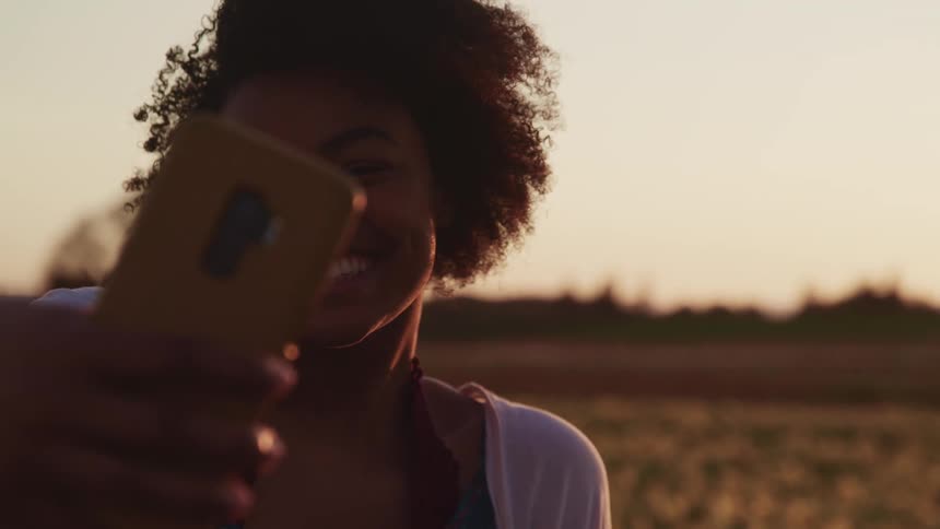 Black woman takes a selfie with a cell phone as she stands in a field