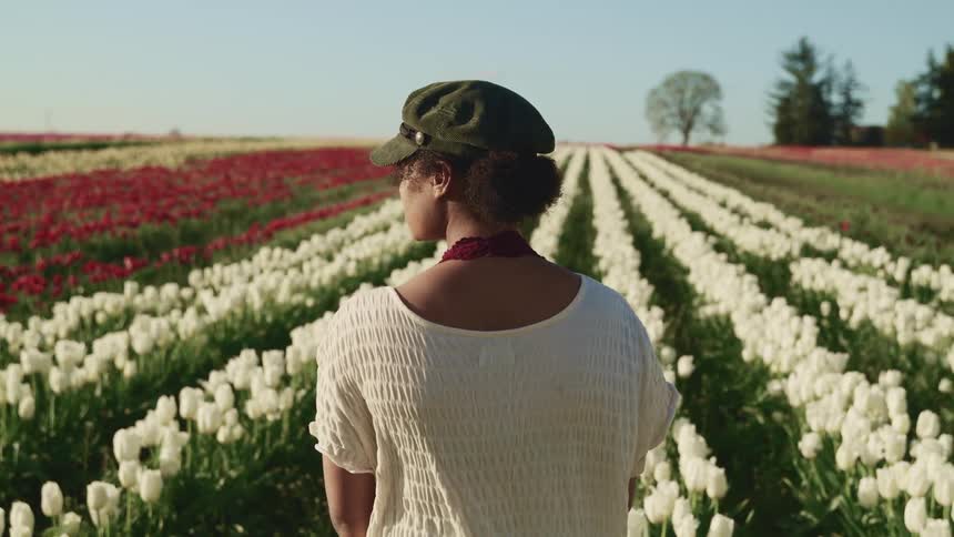 A woman is standing outdoors by a field of flowers