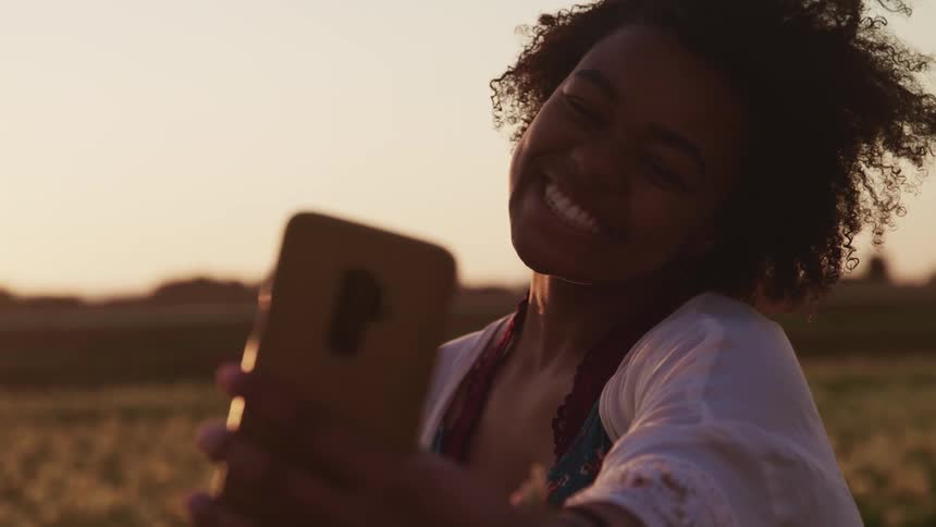 Young woman takes selfies with a smartphone in a tulip field at sunset