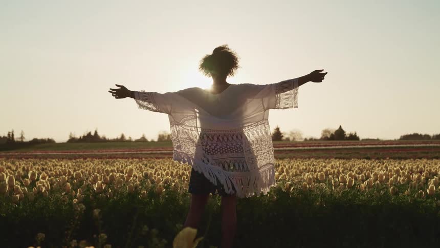 A woman stands in a field with her arms stretched out to her side