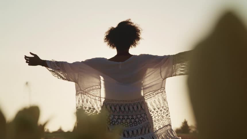 A woman with her arms stretched out to her sides stands in a field