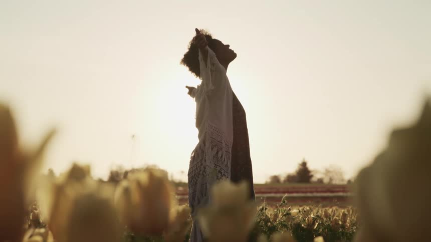 Young woman standing in a tulip fields with arms wide open at sunset