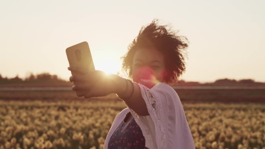 Woman standing in a tulip fields takes selfies with a smartphone at sunset