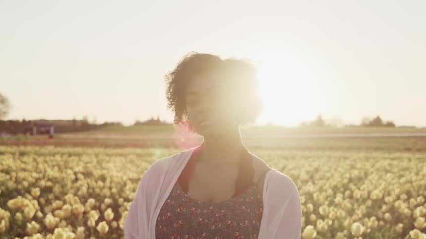 A woman standing in a field of flowers with the sky and clouds in the background