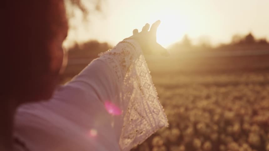 A woman reaches towards the rising sun