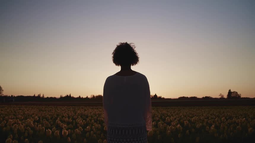 Woman stands in field of tulips face red tinted horizon