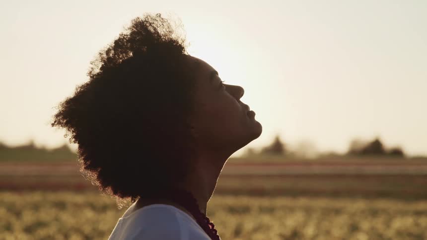 Side view of black woman with curly hair looking up as the sun shines brightly in tulip fields