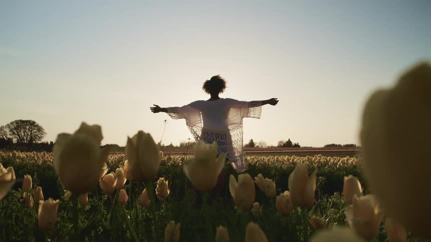 A woman stands in a field of flowers with her arms stretched out to her sides