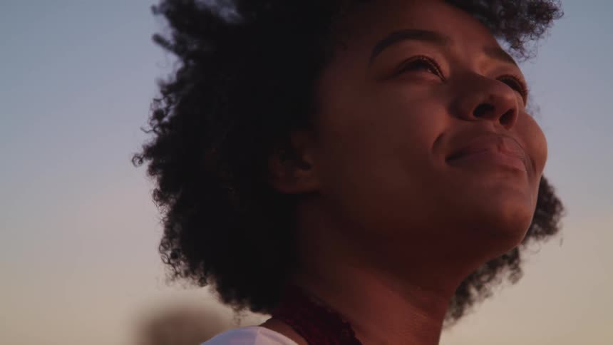 Black woman blinks her eyes as she has her head turned and looks up at the sky