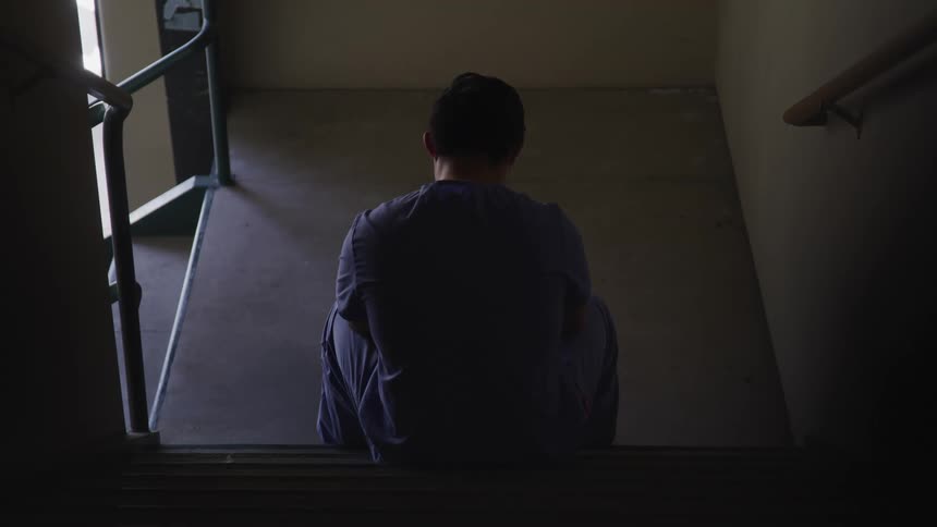 A person with scrubs and a mask sitting on a staircase