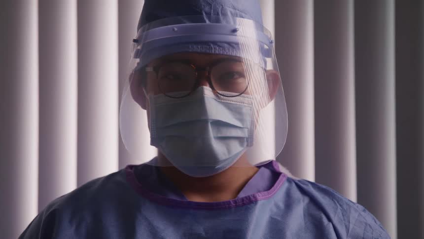 A doctor in surgical gear stares into the camera