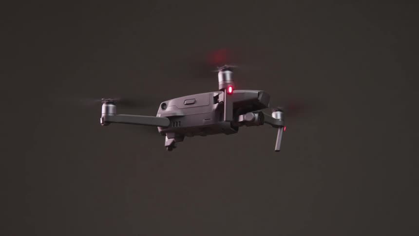 Silver colored drone hovers against dark grey background